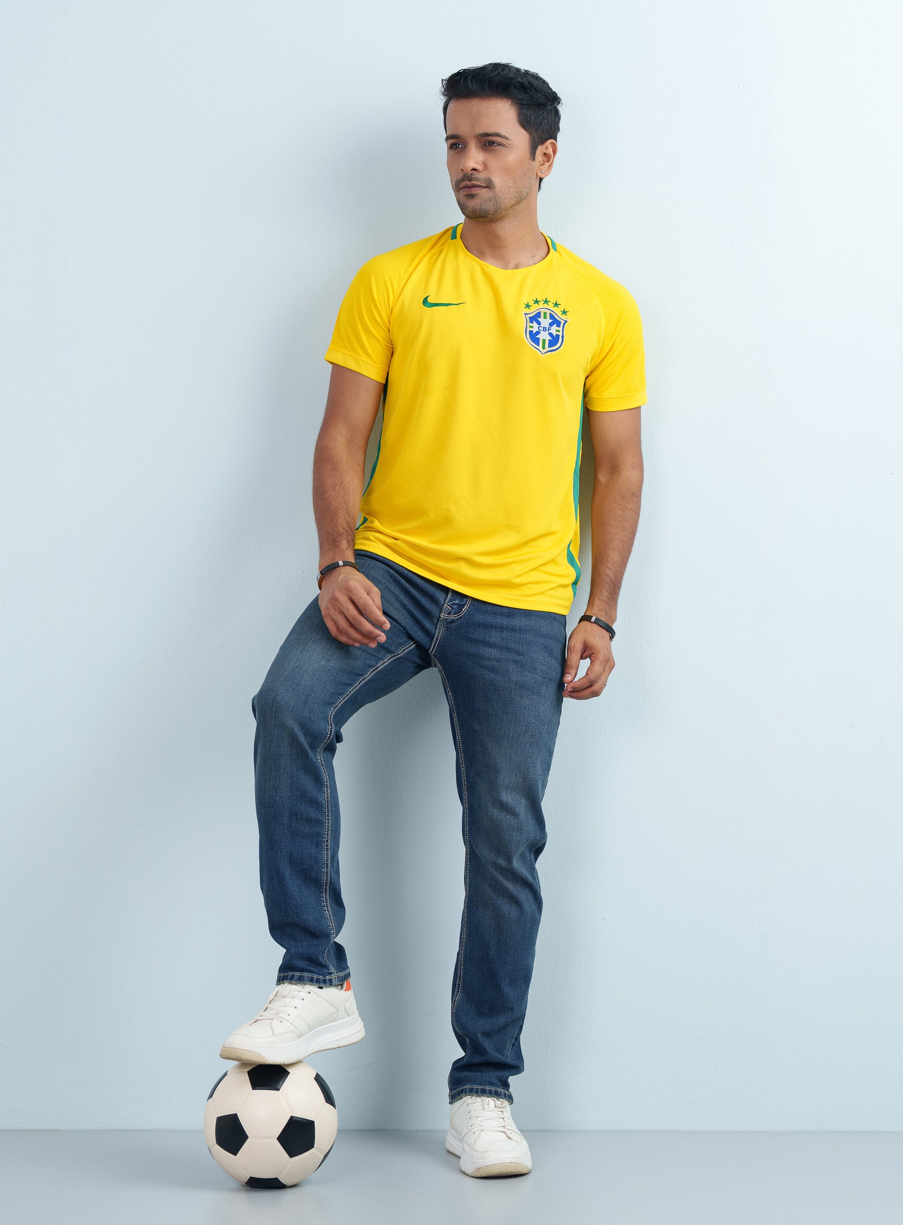 Front view of a man modeling a slim fit cotton mixed Men's Brazil Football Theme Yellow Jersey with blue jeans.