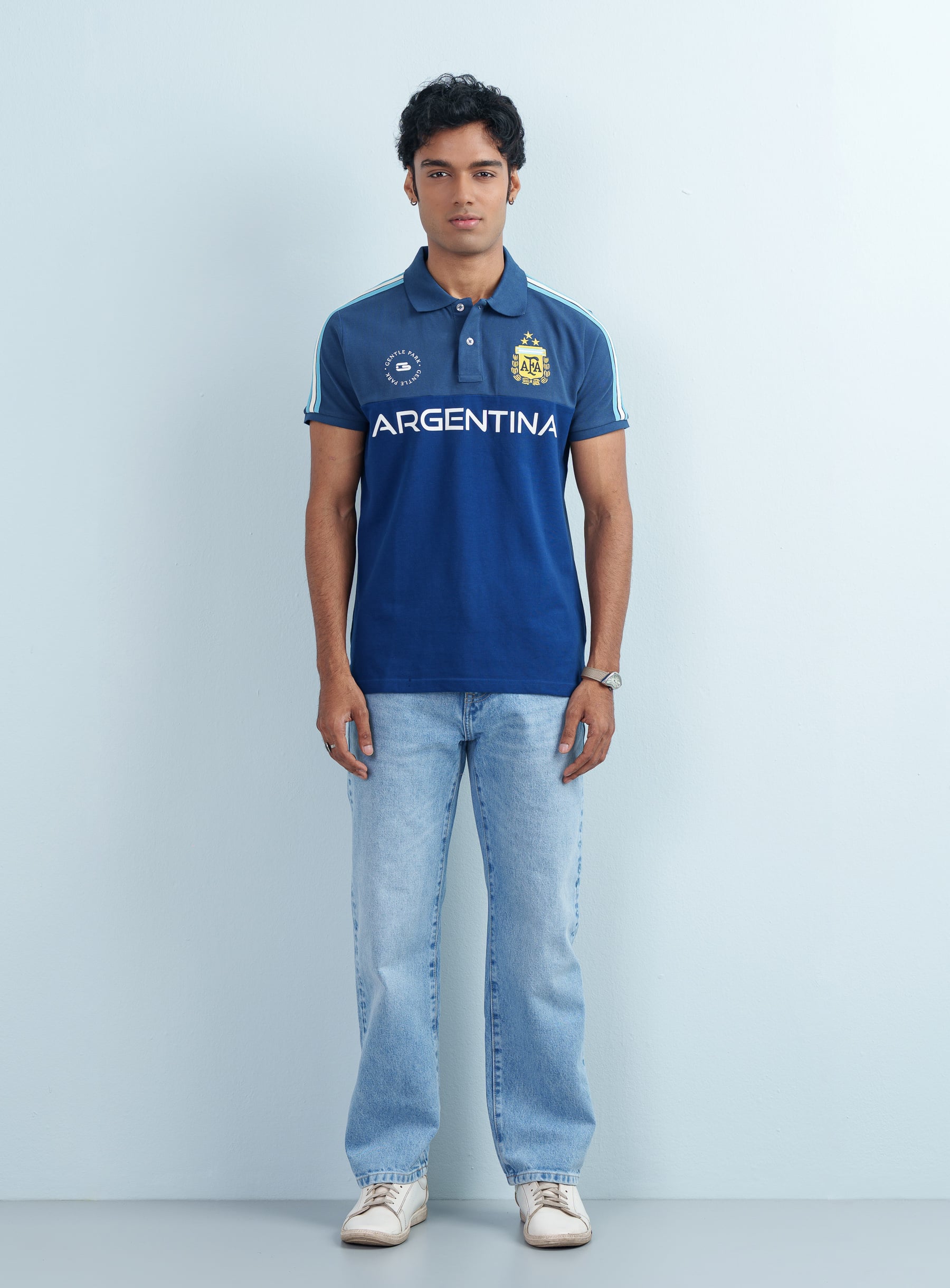 Full-length studio view of a man modeling a men's Argentina Theme Indigo Blue Polo Shirt with light-wash jeans.