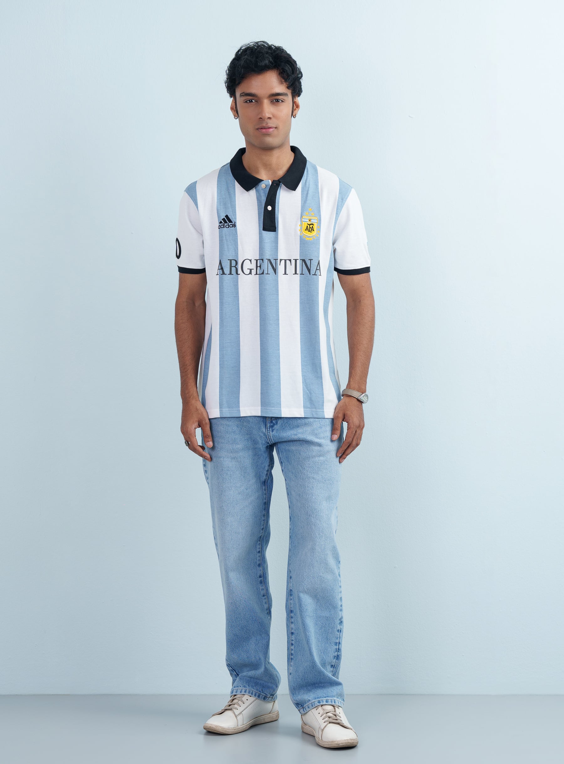 Full length front view of a man wearing a men's Argentina Theme Striped Polo Shirt with light blue jeans.