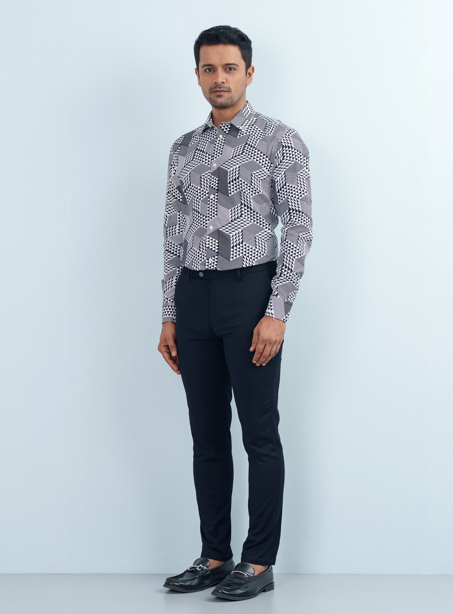 Full-length studio profile view of a model wearing a monochrome triangle pattern formal shirt tucked into black trousers